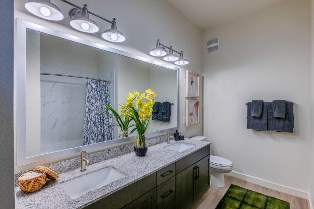 Bathroom area with large mirror, dual sink, granite countertops, wood style flooring, and cool lighting