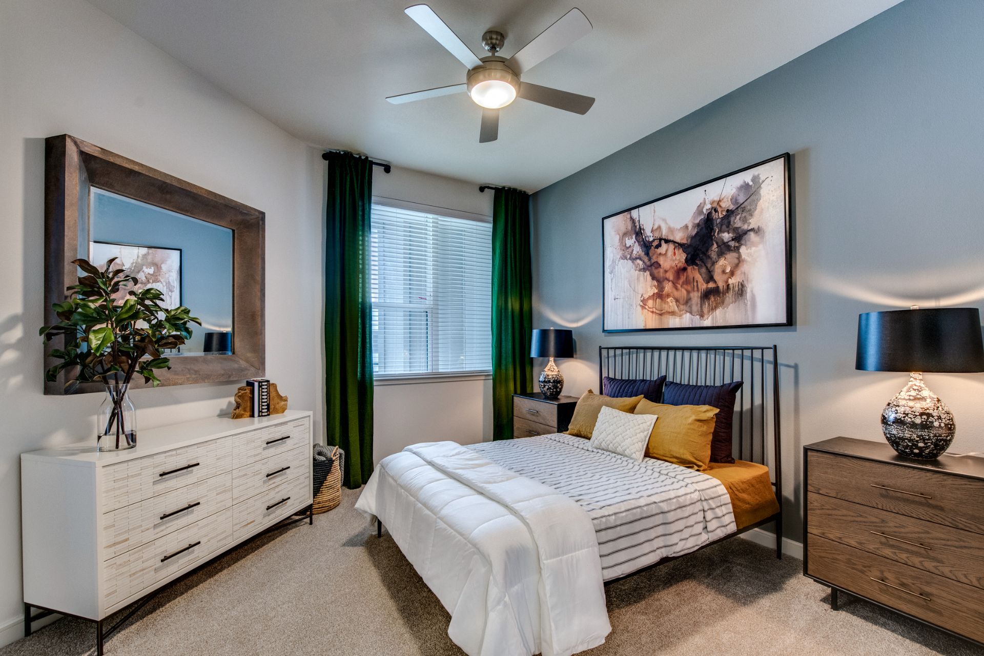 Bedroom area with carpet flooring, mirror, wall paintings, ceiling fan, and warm lighting