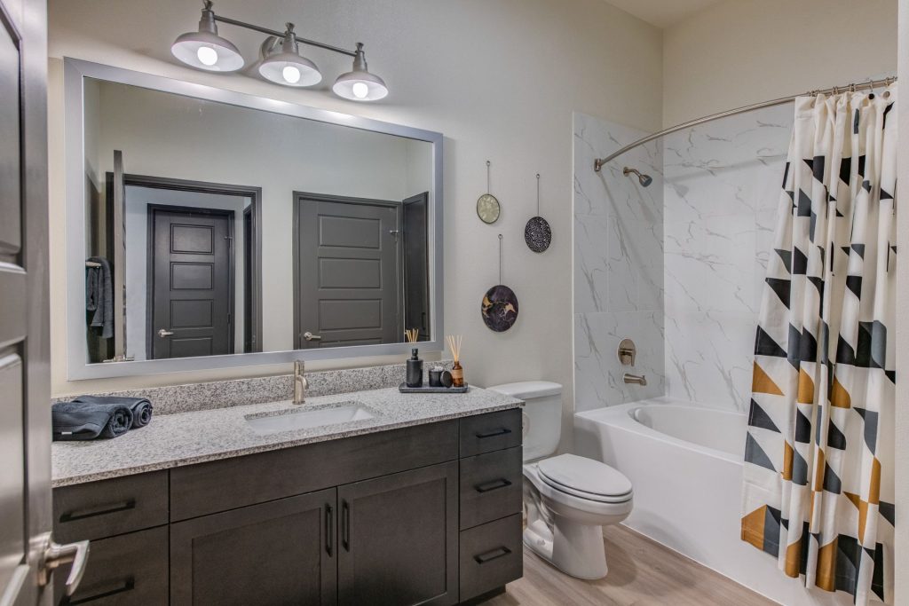 Bathroom area with mirror, single sink, granite countertops, standup shower, wood style flooring, and cool lighting
