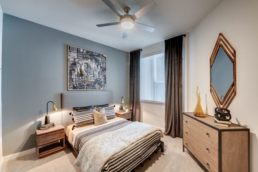 Bedroom area with carpet flooring, mirror, wall paintings, ceiling fan, and warm lighting