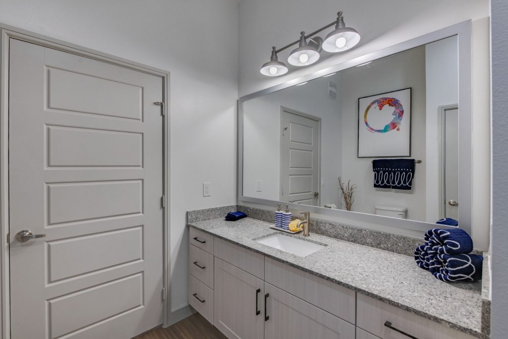 Bathroom area with large mirror, single sink, granite countertops, wood style flooring, and cool lighting