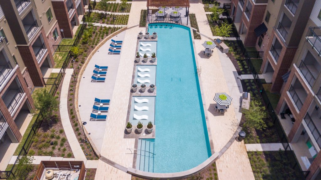 Aerial view of outdoor pool area with shaded seating, sun tan chairs, tropical landscaping, and grilling stations