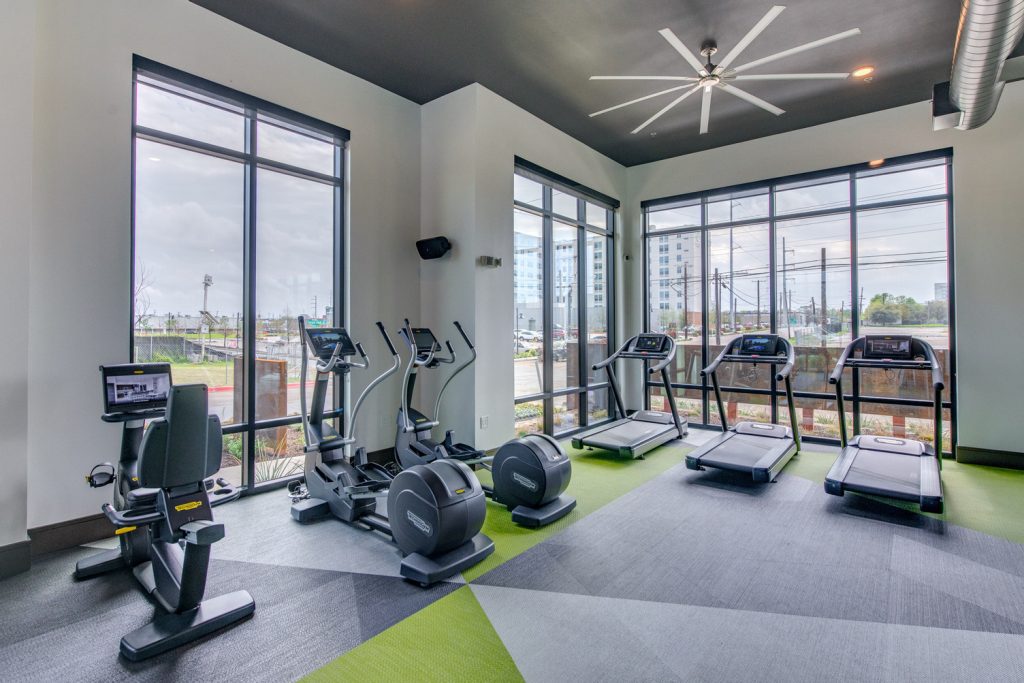 Indoor gym area with workout machines, weights, floor to ceiling windows, and ceiling fans