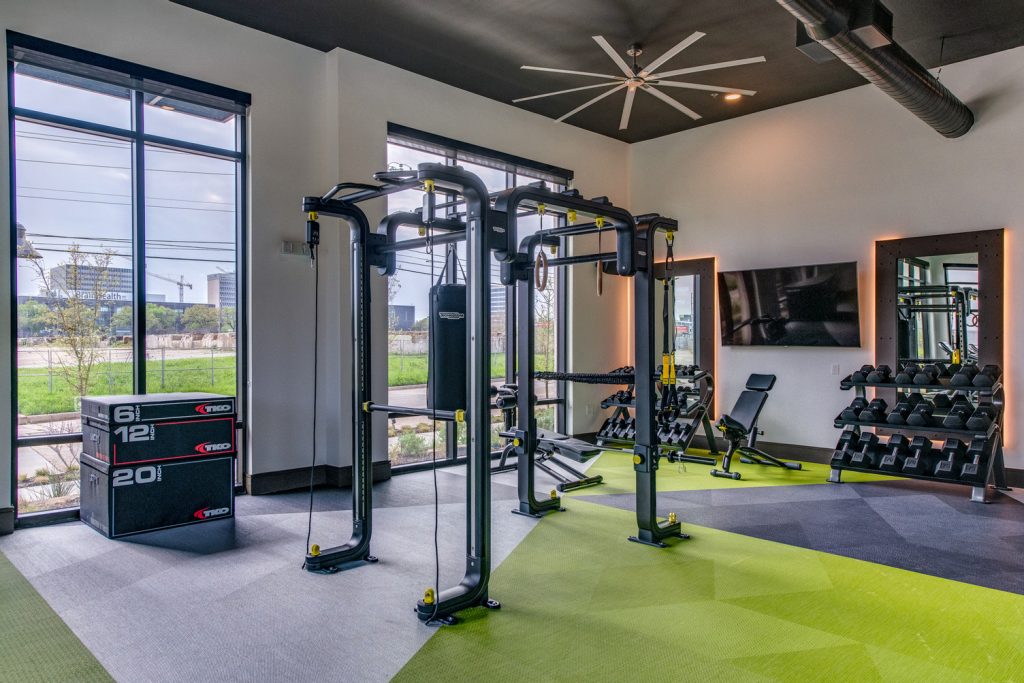 Indoor gym area with workout machines, weights, floor to ceiling windows, television, and ceiling fans