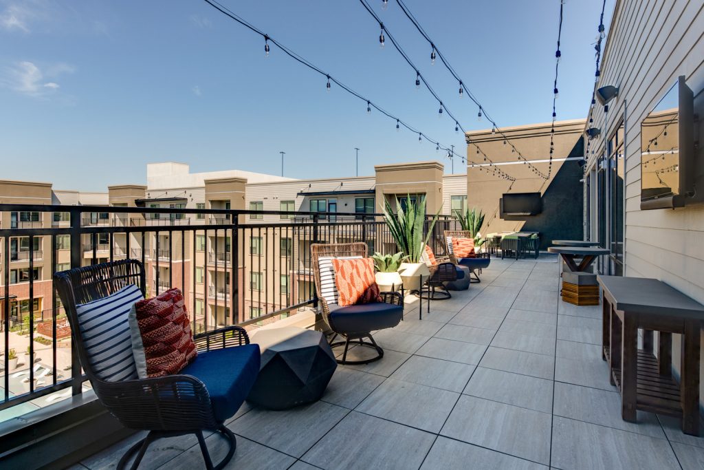 Wide view Rooftop patio with string lights, large wall mounted televsions, seating, and various planters, as well as wall art