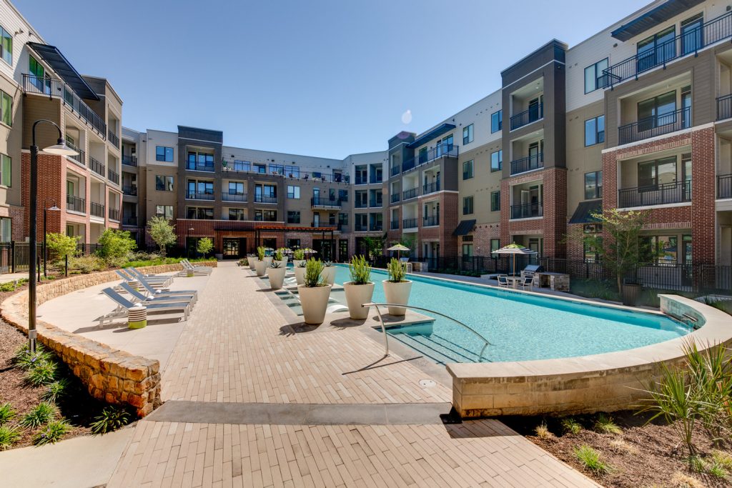 Outdoor pool area with shaded seating, sun tan chairs, tropical landscaping, and grilling stations