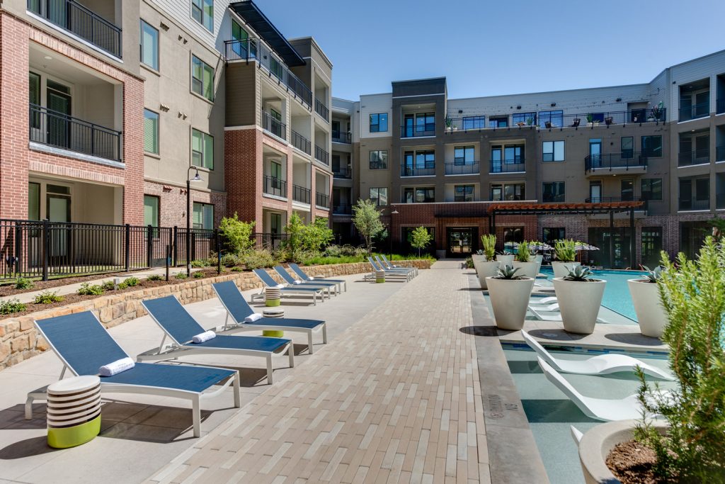 Outdoor pool area with shaded seating, sun tan chairs, tropical landscaping, and grilling stations