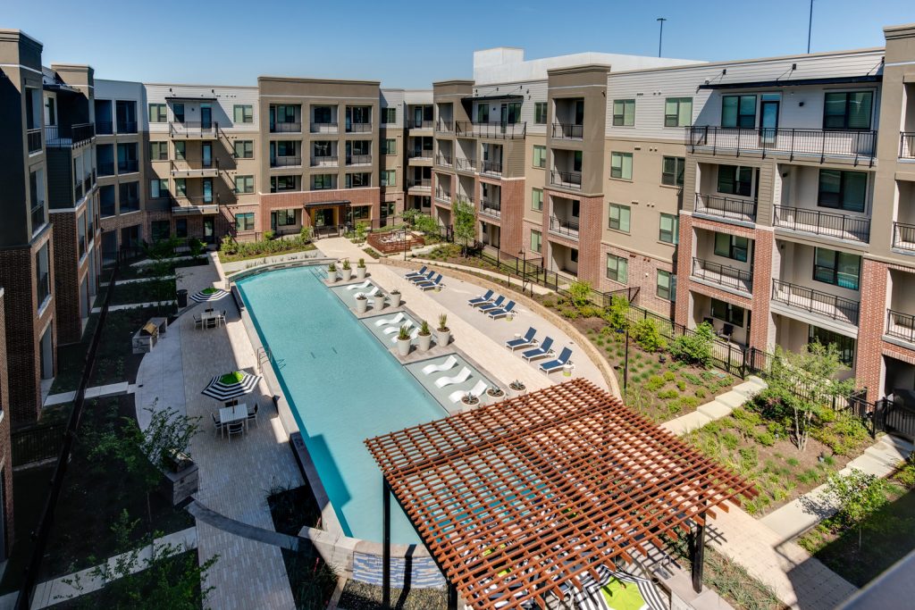 Aerial view of outdoor pool area with shaded seating, sun tan chairs, tropical landscaping, and grilling stations