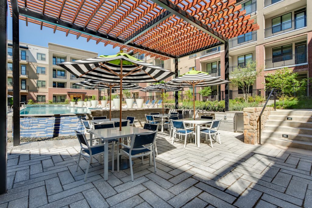 Outdoor pool area with shaded seating, sun tan chairs, tropical landscaping, and grilling stations