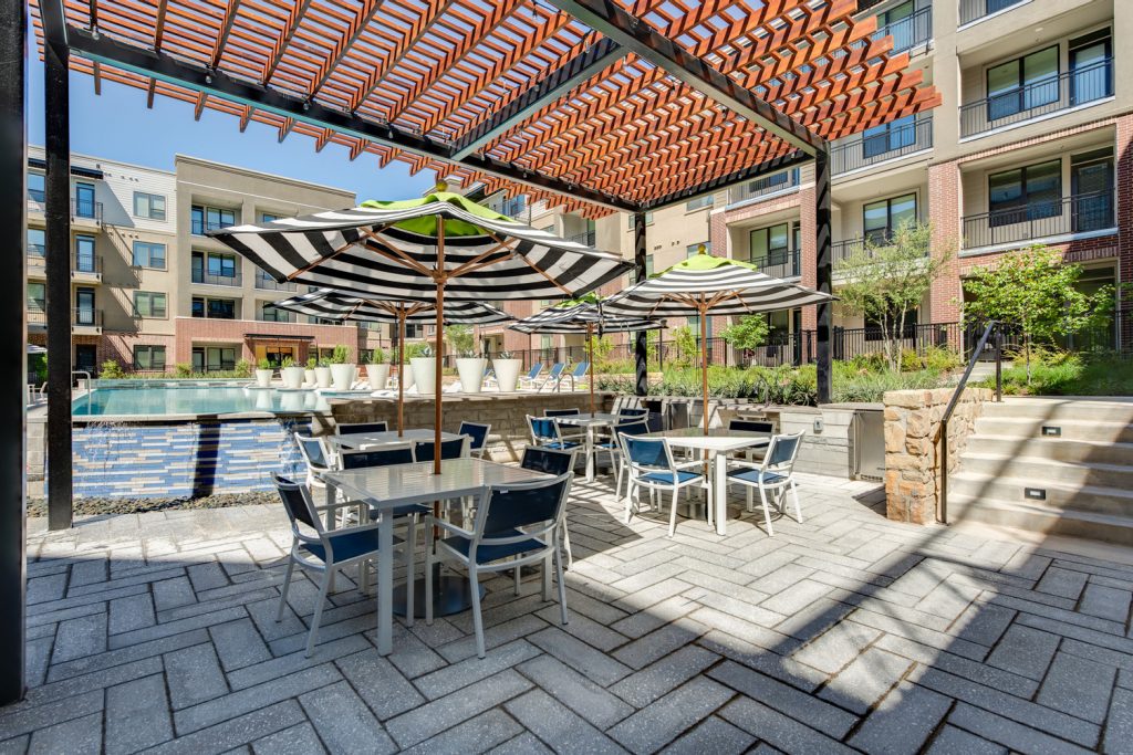 Outdoor pool area with shaded seating, sun tan chairs, tropical landscaping, and grilling stations