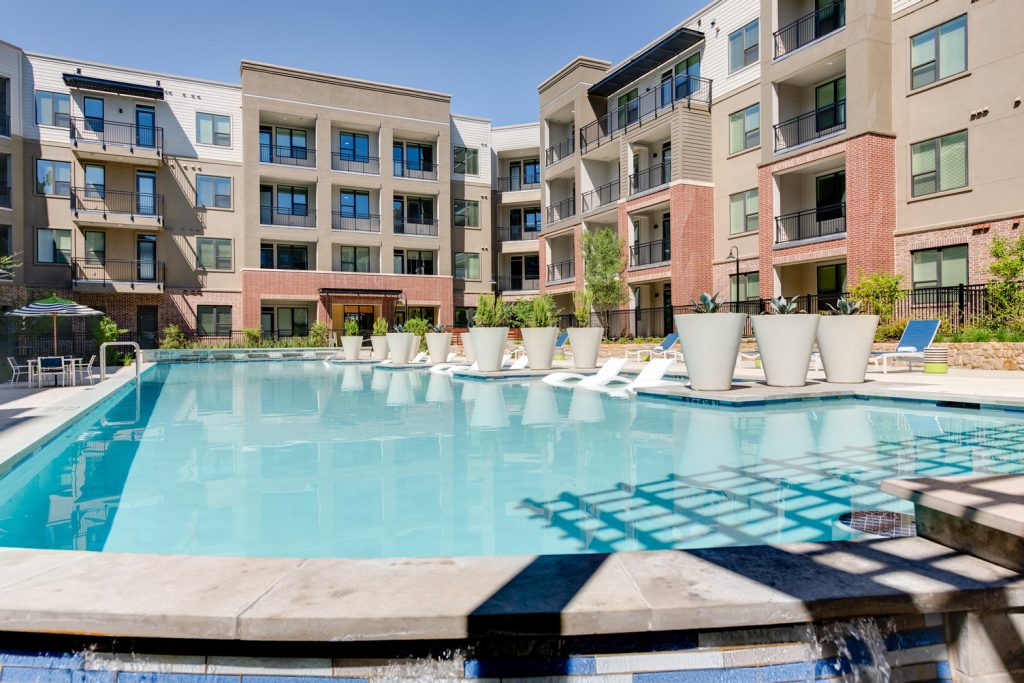 Outdoor pool area with shaded seating, sun tan chairs, tropical landscaping, and grilling stations