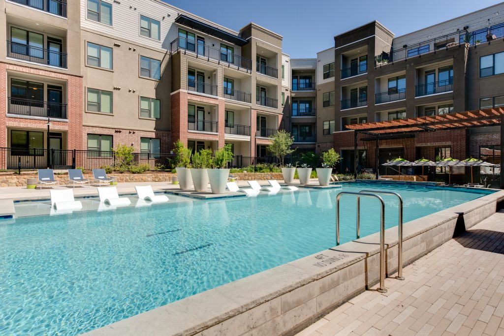 Outdoor pool area with shaded seating, sun tan chairs, tropical landscaping, and grilling stations